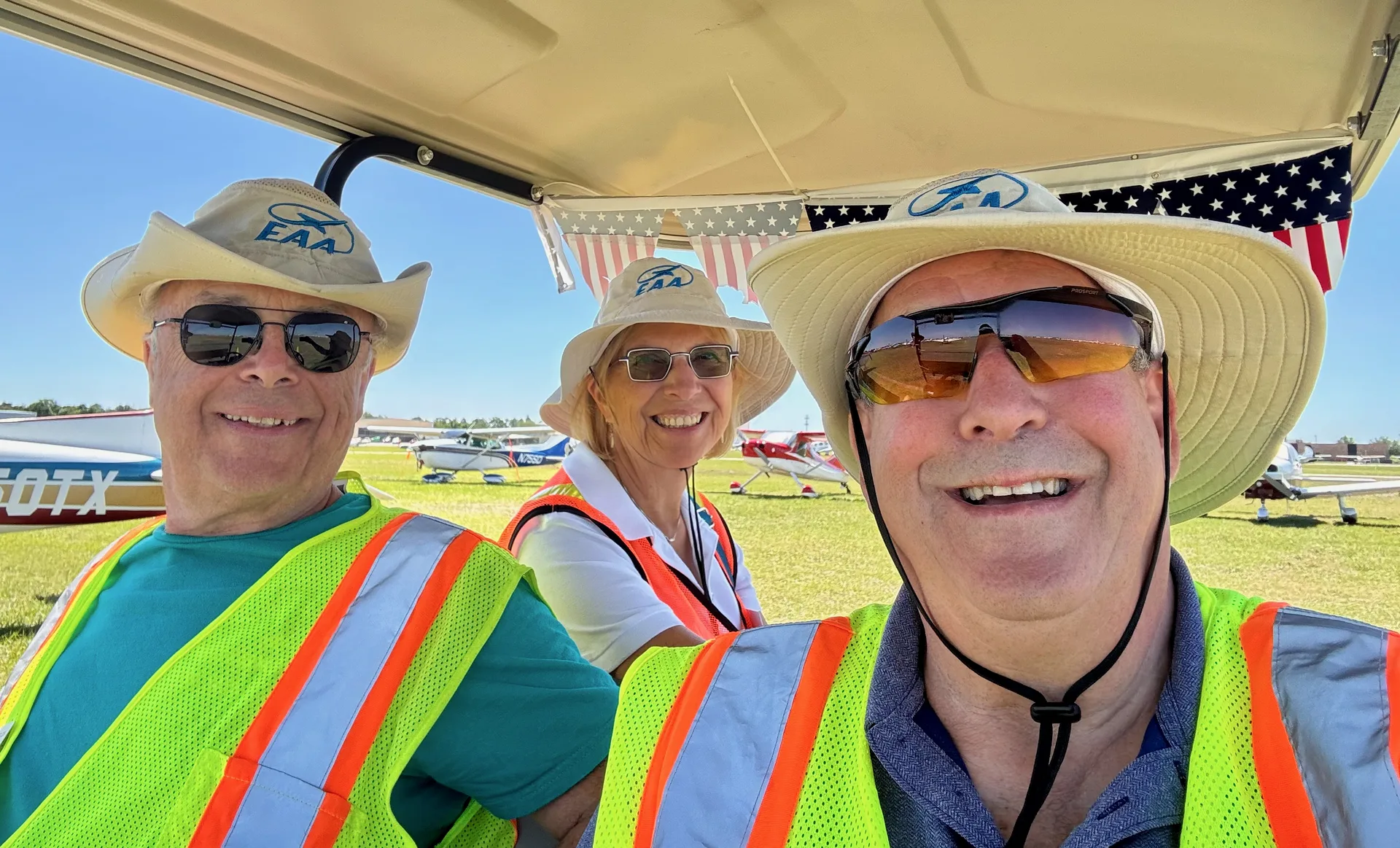 EAA Chapter 229 volunteers riding the tie-down golf cart decorated with American flag bunting at Sun n Fun 2026