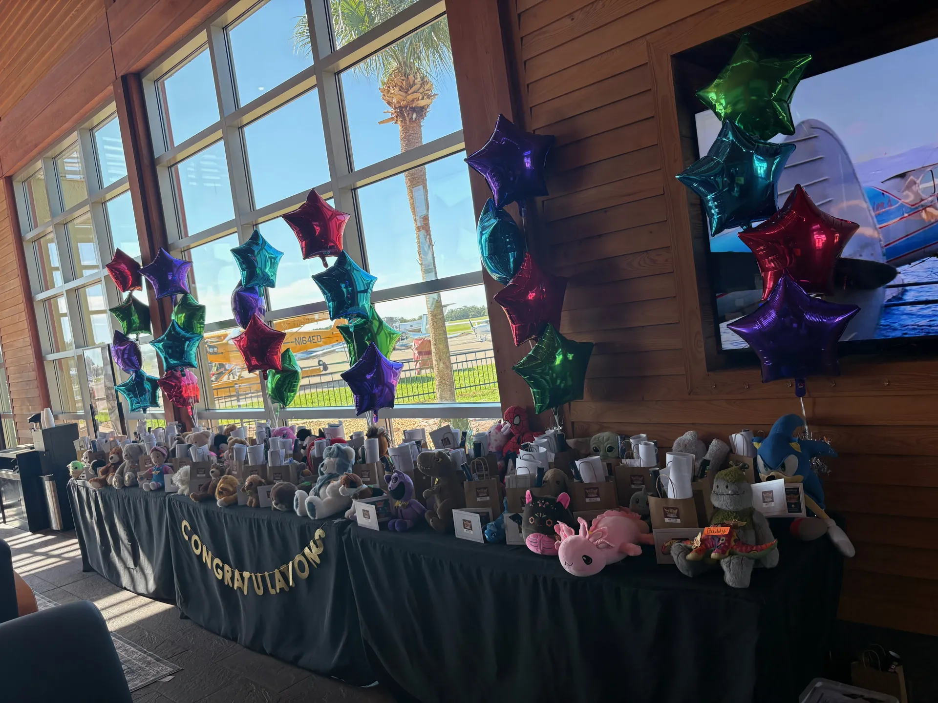 Stuffed animal graduates lined up under balloons and a Congratulations banner, ready for pickup