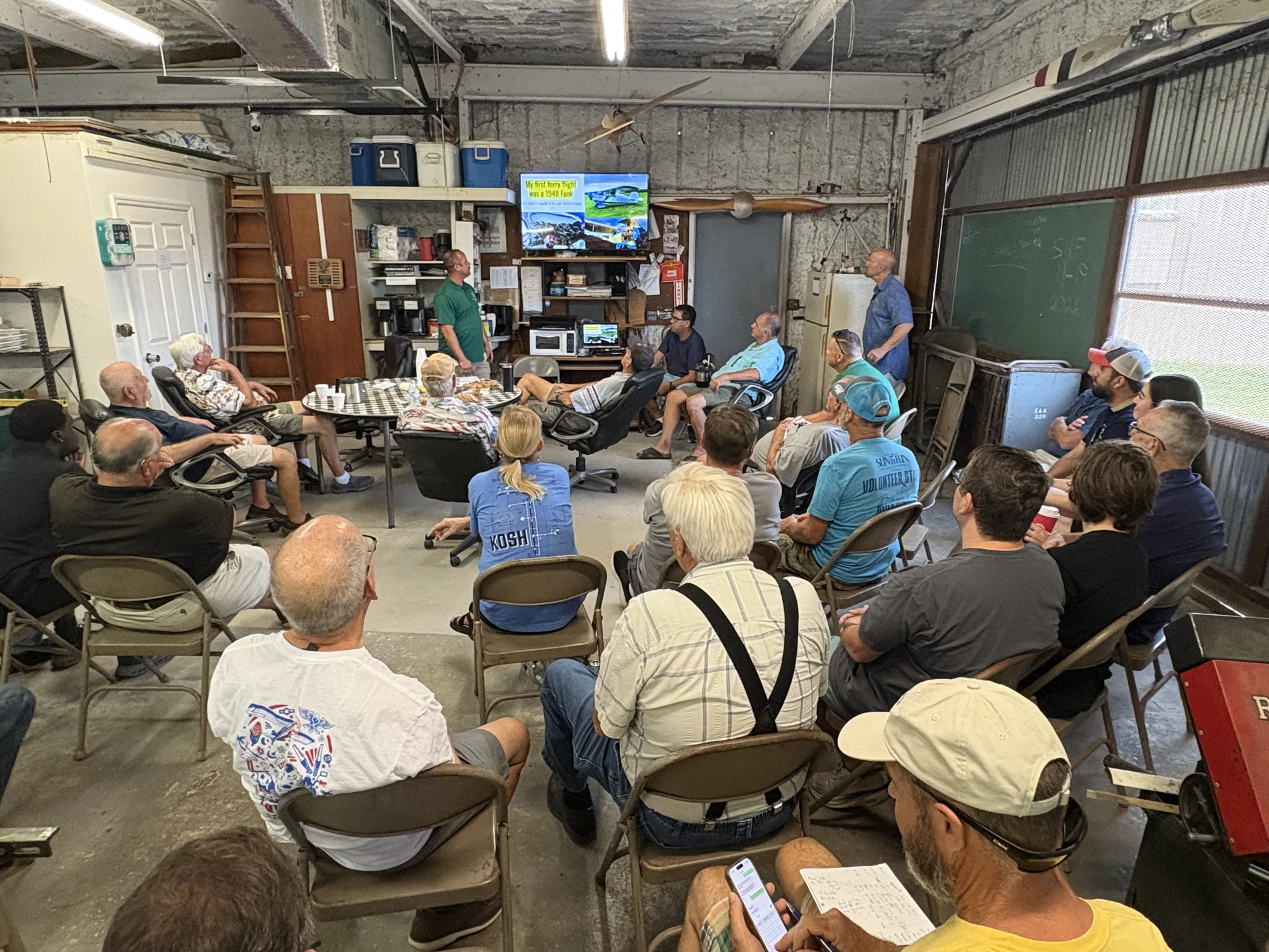 Members gathered around the table at the back of Hangar 100 under the American flag